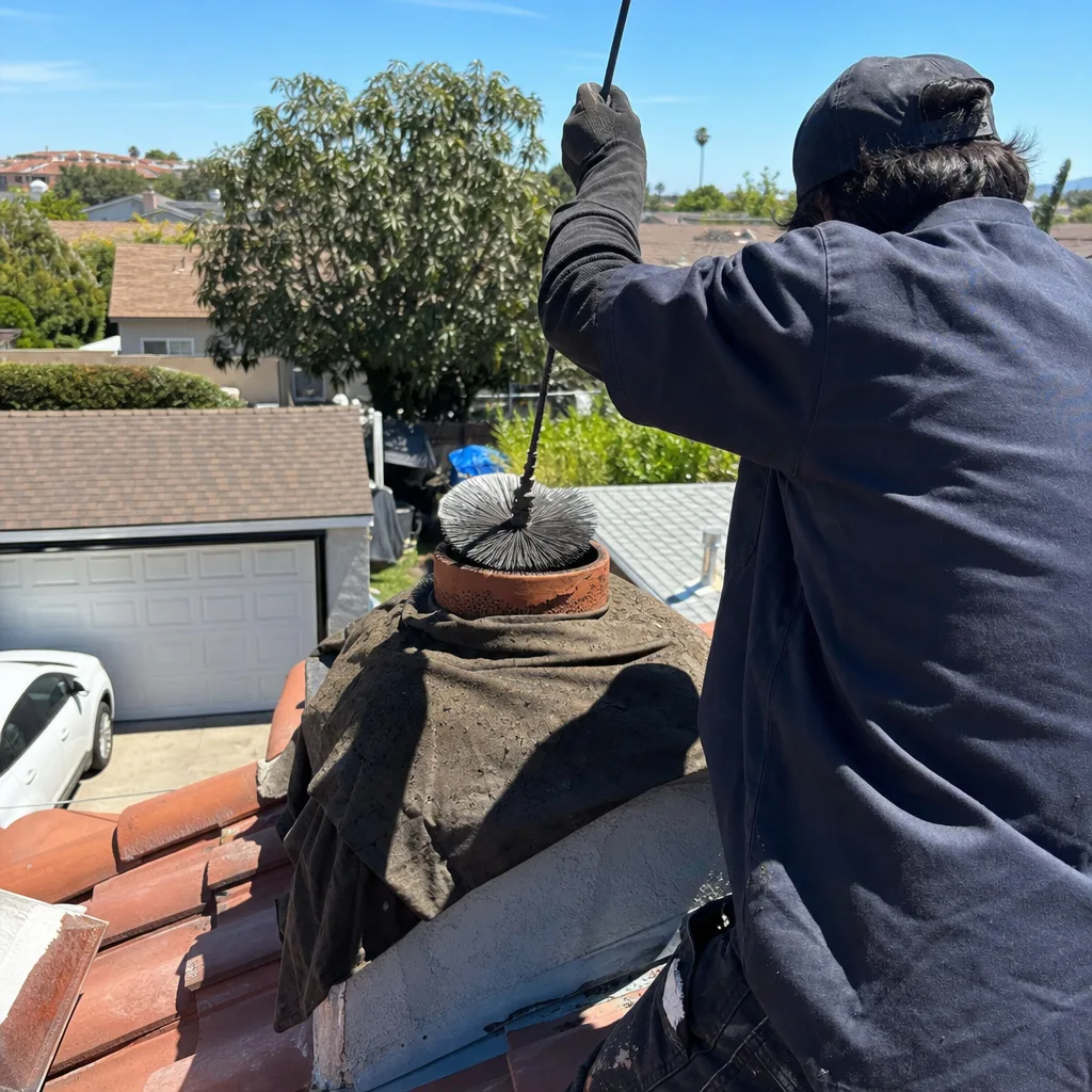 Professional chimney sweep cleaning a rooftop chimney with a wire brush.